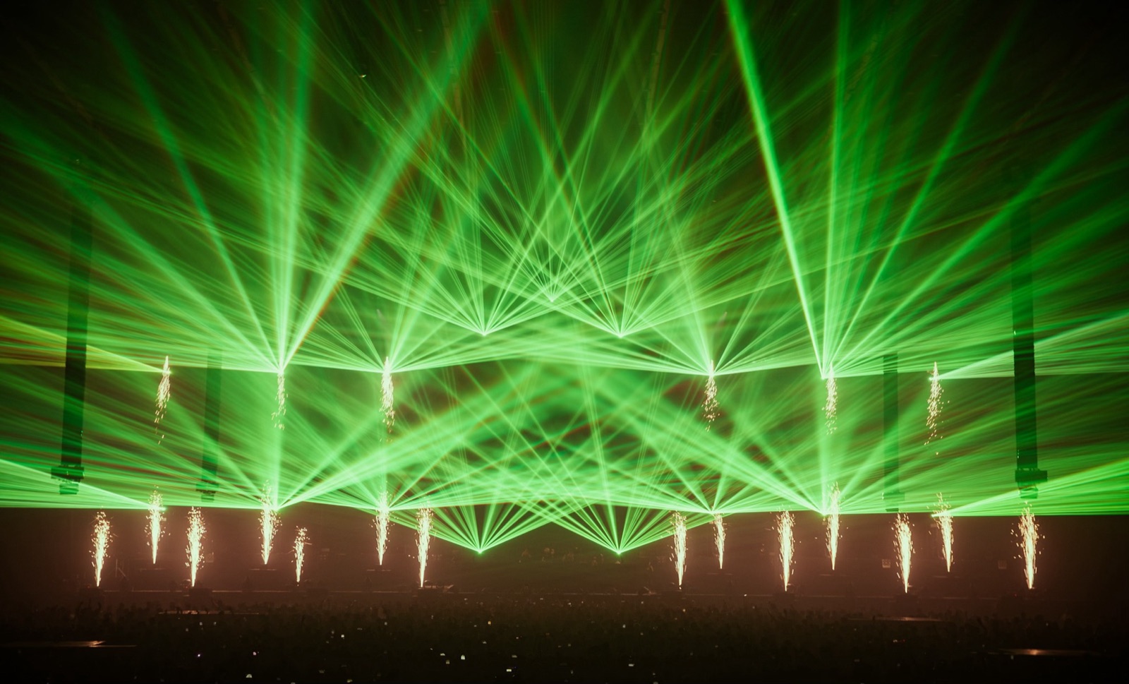 Groene laserwaaiers boven een festivalpodium, met vonkenfonteinen (Sparkular) eronder, 2025